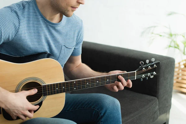 Vue recadrée du musicien assis sur le canapé et jouant de la guitare acoustique à la maison — Photo de stock