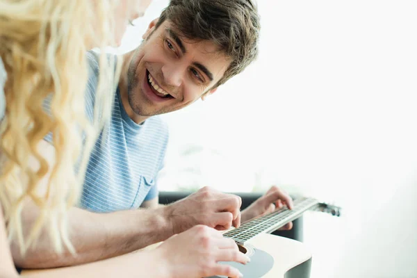 Cheerful man holding acoustic guitar and looking at blonde woman — Stock Photo
