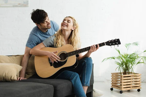 Felice donna bionda che suona la chitarra acustica vicino all'uomo allegro — Foto stock