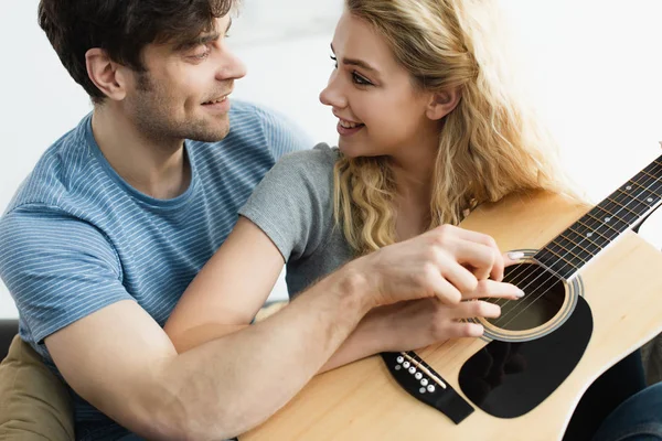 Hombre feliz y mujer rubia alegre tomados de las manos de cuerdas y mirándose el uno al otro - foto de stock