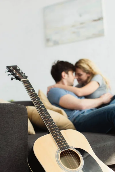 Selektiver Fokus der Akustikgitarre in der Nähe eines glücklichen Paares, das sich zu Hause umarmt — Stockfoto