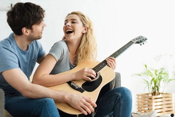 Felice bionda giovane donna che tiene la chitarra acustica vicino all'uomo allegro — Foto stock