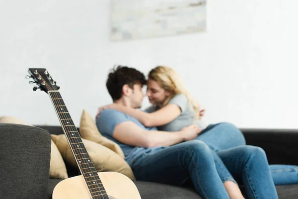 Selective focus of acoustic guitar near cheerful couple hugging at home — Stock Photo