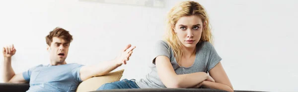 Panoramic shot of offended blonde woman sitting on sofa near man — Stock Photo