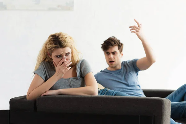 Selective focus of offended blonde woman covering face near man gesturing in living room — Stock Photo