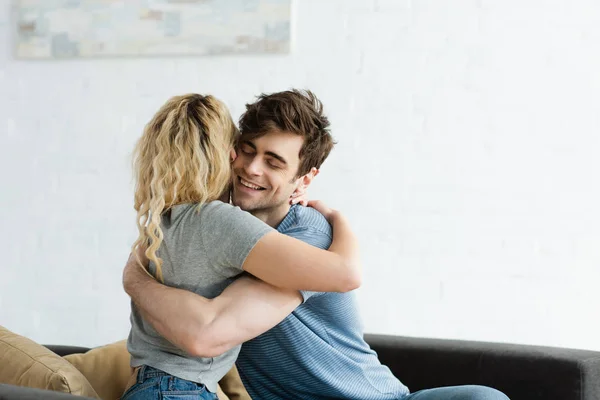 Hombre feliz sonriendo mientras abraza chica rubia en casa - foto de stock