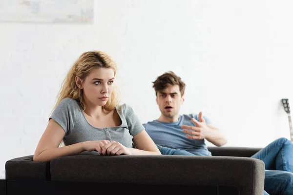 Селективное внимание обиженной блондинки, сидящей на диване рядом с мужчиной — стоковое фото