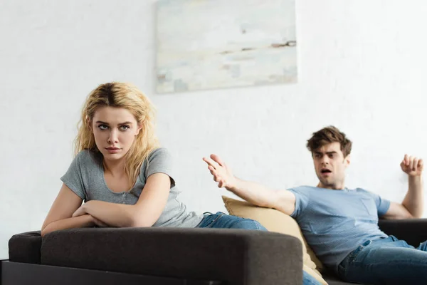 Selective focus of frustrated blonde woman with crossed arms near man gesturing in living room — Stock Photo