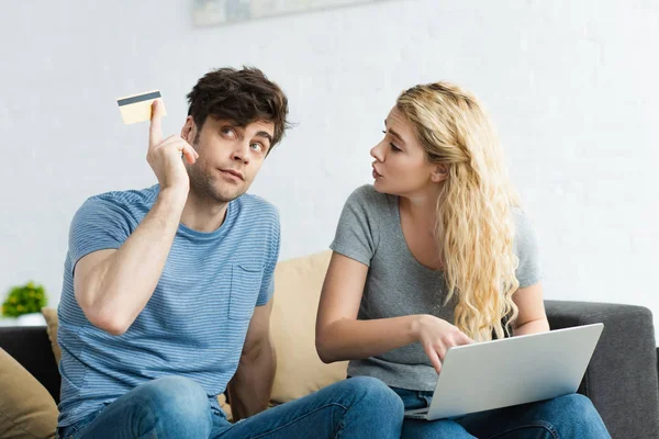 Attractive blonde girl using laptop and talking with man holding credit card — Stock Photo