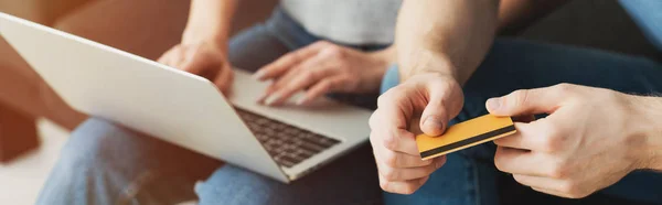 Plano panorámico de la mujer usando el ordenador portátil cerca del hombre con tarjeta de crédito - foto de stock