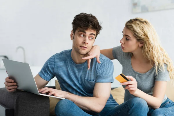 Блондинка вказує пальцем на ноутбук біля чоловіка, що тримає кредитну картку — стокове фото