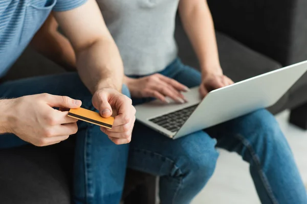 Обрезанный вид мужчины, держащего кредитную карту рядом с молодой женщиной с помощью ноутбука — стоковое фото