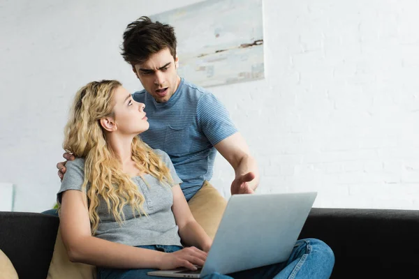 Schöner Mann gestikuliert beim Blick auf Laptop in der Nähe blondes Mädchen — Stockfoto