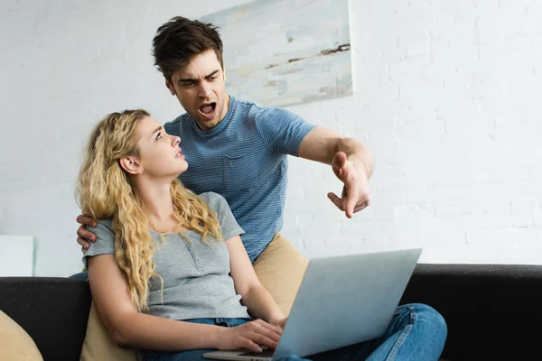 Uomo emotivo gesticolando guardando il computer portatile vicino alla ragazza bionda — Foto stock