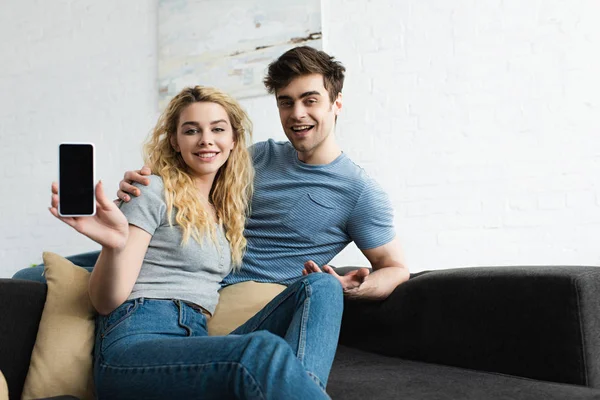 Cheerful man sitting with blonde woman holding smartphone with blank screen — Stock Photo