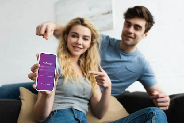 Selektiver Fokus von fröhlichem Mann und blonder Frau, die mit den Fingern auf das Smartphone zeigen, mit Instagram-App auf dem Bildschirm — Stockfoto