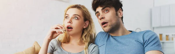 Panoramic shot of shocked man watching movie near blonde girl holding popcorn — Stock Photo