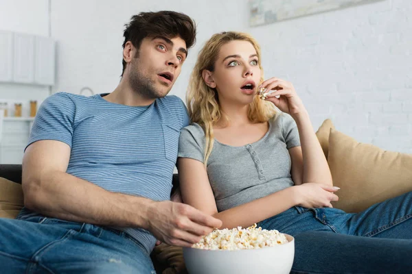 Schockierter Mann sieht Film nahe blondem Mädchen und Schüssel mit Popcorn — Stockfoto