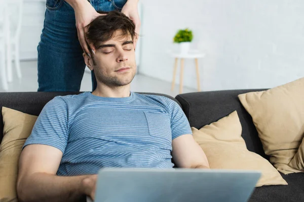 Abgeschnittene Ansicht einer Frau, die den Kopf eines hübschen Mannes berührt, der auf dem Sofa sitzt — Stockfoto