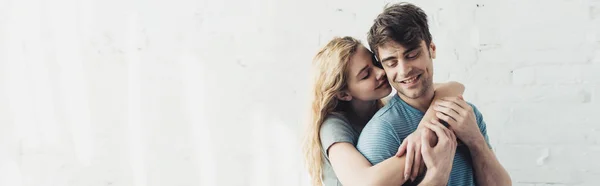 Panoramic shot of blonde cheerful girl hugging handsome and happy boyfriend — Stock Photo