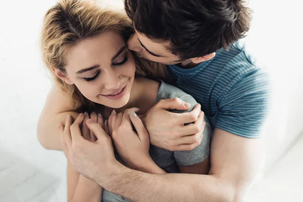 Guapo hombre besando mejilla de joven feliz mujer con los ojos cerrados - foto de stock