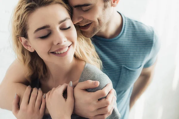 Cheerful and handsome man hugging young happy woman with closed eyes — Stock Photo