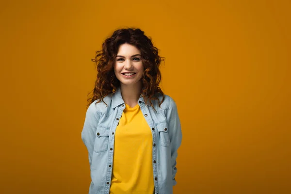 Happy curly redhead woman looking at camera and smiling on orange — Stock Photo