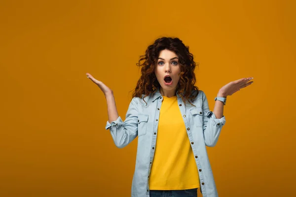 Shocked curly redhead woman looking at camera and gesturing on orange — Stock Photo