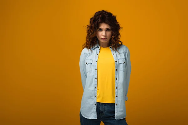 Upset curly redhead woman looking at camera and standing on orange — Stock Photo