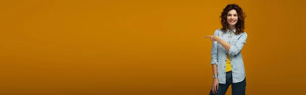 Панорамний знімок веселого кучерявого рудої жінки, що стоїть і вказує пальцем на апельсин — стокове фото
