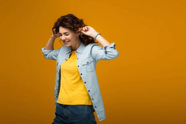 Alegre pelirroja mujer tapando orejas mientras de pie en naranja - foto de stock