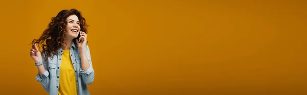 Plano panorámico de atractiva pelirroja rizada hablando en el teléfono inteligente en naranja - foto de stock