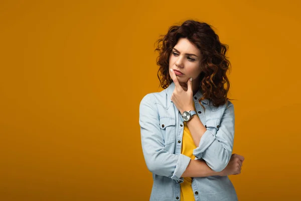 Pensive curly redhead woman touching lips while thinking on orange — Stock Photo