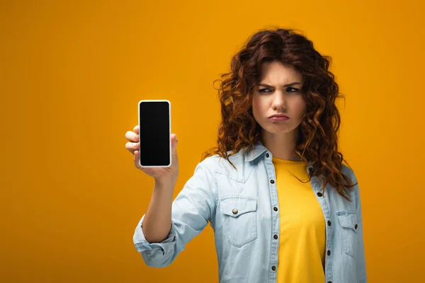 Расстроена женщина держит смартфон с пустым экраном на оранжевом — стоковое фото