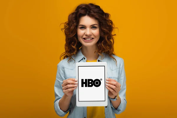 Щасливий Рудий Жінка тримає цифровий планшет з додатком HBO на екрані, стоячи на помаранчевому — стокове фото
