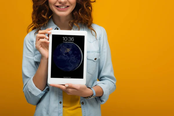 Vista ritagliata di allegra ragazza riccia in possesso di tablet digitale con schermo di blocco isolato su arancione — Foto stock