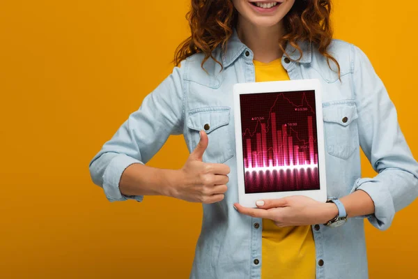Обрезанный вид кудрявая девушка держит цифровой планшет с диаграммами и графиками и показывает большой палец вверх изолированы на оранжевый — стоковое фото