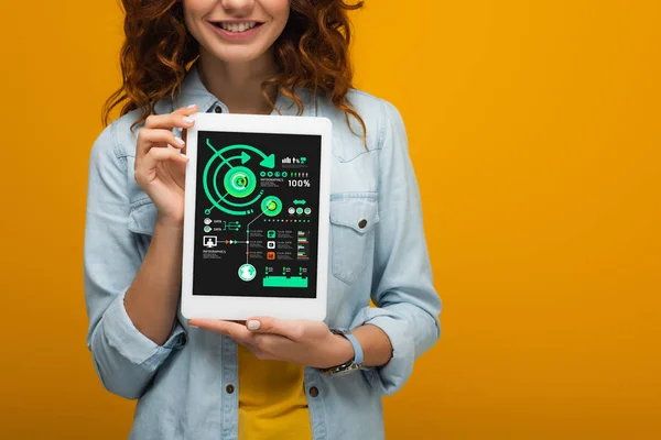 Cropped view of curly girl holding digital tablet with charts and graphs isolated on orange — Stock Photo