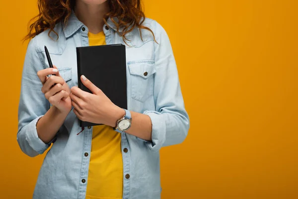 Cropped view of young woman holding notebook and pen on orange — Stock Photo