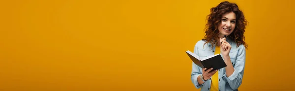 Foto panorámica de la joven pelirroja feliz sosteniendo el cuaderno y la pluma en naranja - foto de stock