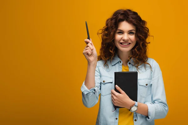 Feliz ruiva jovem segurando notebook e caneta em laranja — Fotografia de Stock