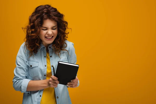 Rossa emotiva giovane donna in possesso di notebook e penna arancione — Foto stock