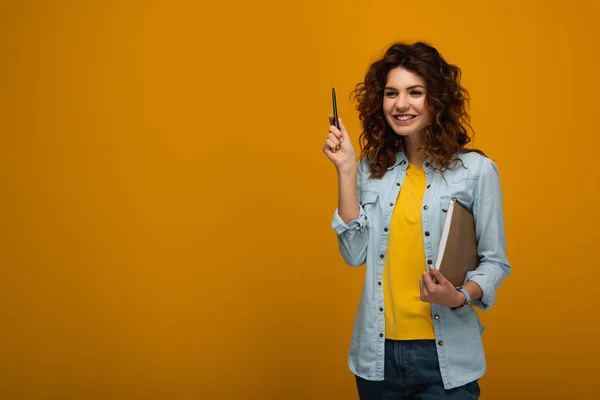 Beautiful redhead young woman holding notebook and pen on orange — Stock Photo