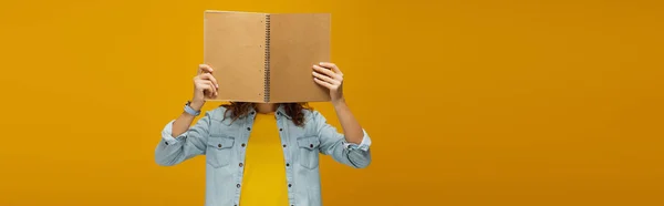 Colpo panoramico di giovane donna che copre il viso con notebook su arancione — Foto stock