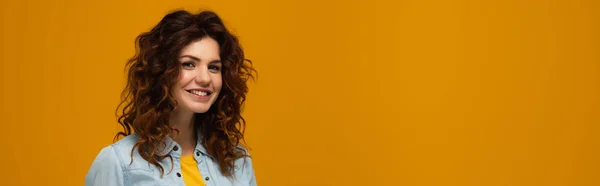 Panoramic shot of young curly woman looking at camera isolated on orange — Stock Photo