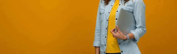 Colpo panoramico di giovane donna in piedi e tenendo il computer portatile isolato su arancione — Foto stock