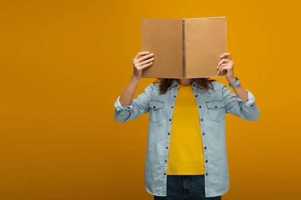 Young woman standing and covering face with notebook on orange — Stock Photo