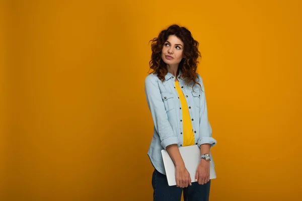 Beautiful pensive redhead girl holding laptop on orange — Stock Photo