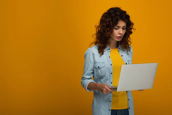 Upset curly redhead girl using laptop on orange — Stock Photo