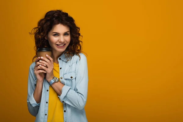 Щаслива кучерява руда дівчина тримає паперову чашку, посміхаючись на апельсині — стокове фото